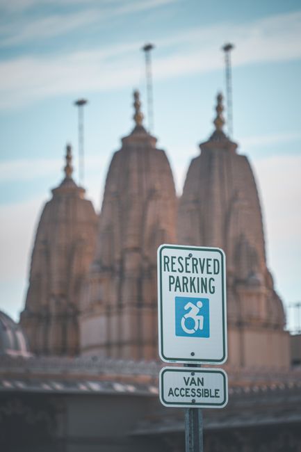 A dedicated parking sign indicating reserved parking for disabled individuals, featuring a blue wheelchair symbol on a white background. The sign is mounted on a metal pole situated in an urban enviro